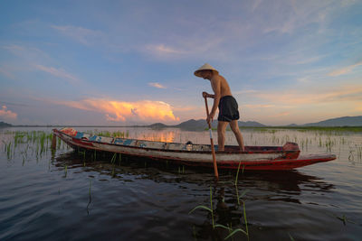 Man standing in boat against sky during sunset