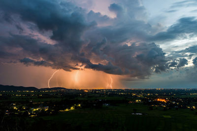 Scenic view of illuminated city against dramatic sky during sunset