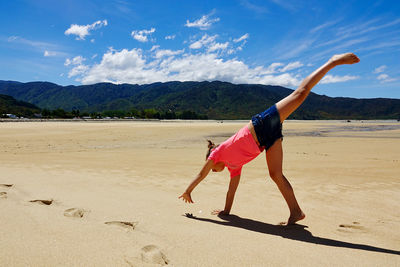 Full length of girl doing a cartwheel on deserted beach against sky