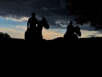 Silhouette men sitting on land against sky during sunset