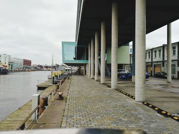 Footpath by street in city against sky