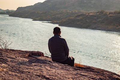 Isolated man sitting at mountain top with lake view backbit shot from flat angle