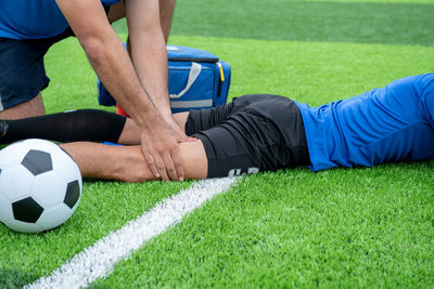 Low section of male physical therapist rubbing soccer player leg on field