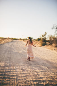 Rear view of woman with umbrella on road against clear sky