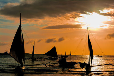 Silhouette outrigger sailing boats on sea against sky during sunset