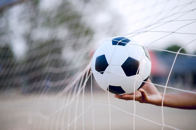 Cropped hand holding soccer ball by net outdoors