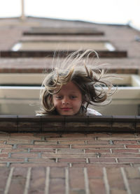 Low angle portrait of girl leaning from building