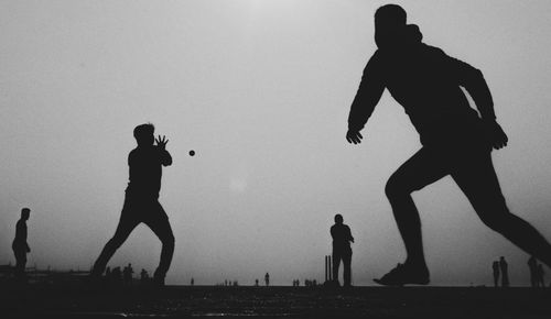 Silhouette people playing cricket against clear sky