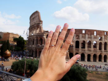 Close-up of hand against historic building against sky