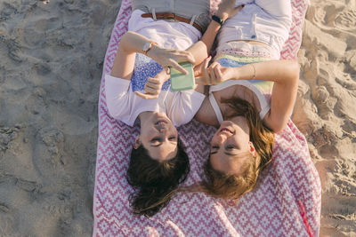 Women using mobile phone while lying on picnic blanket at beach