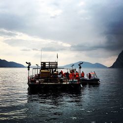 Workers in boat sailing in lake iseo against sky