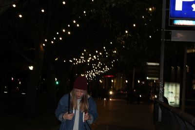 Woman standing on illuminated street at night