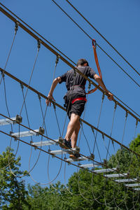 Low angle view of man walking on rope against sky