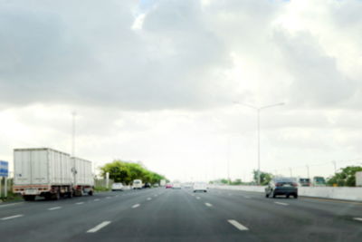 Vehicles on road against cloudy sky