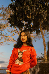 Portrait of young woman standing against trees