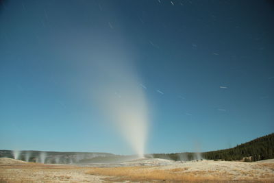 Old faithful geyser erupting at night under the stars and lit by a full moon. 