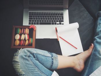 Low section of woman with macaroons by book and laptop on bed