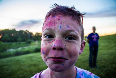 Close-up portrait of boy covered in powder paint on field against sky
