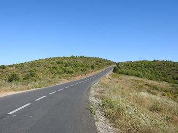 Road along countryside landscape against clear blue sky