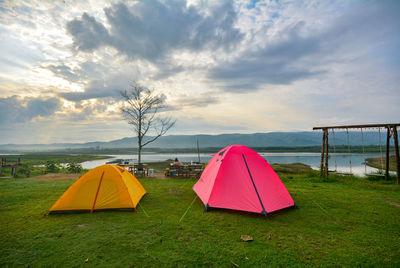 Tents at lakeshore against cloudy sky during sunset