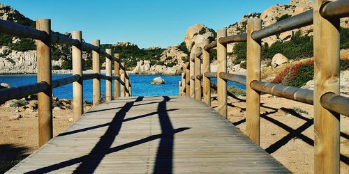 Walkway by sea against clear blue sky