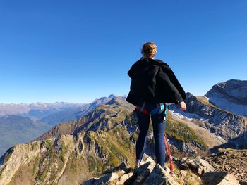 Rear view of young woman standing on mountain against clear blue sky