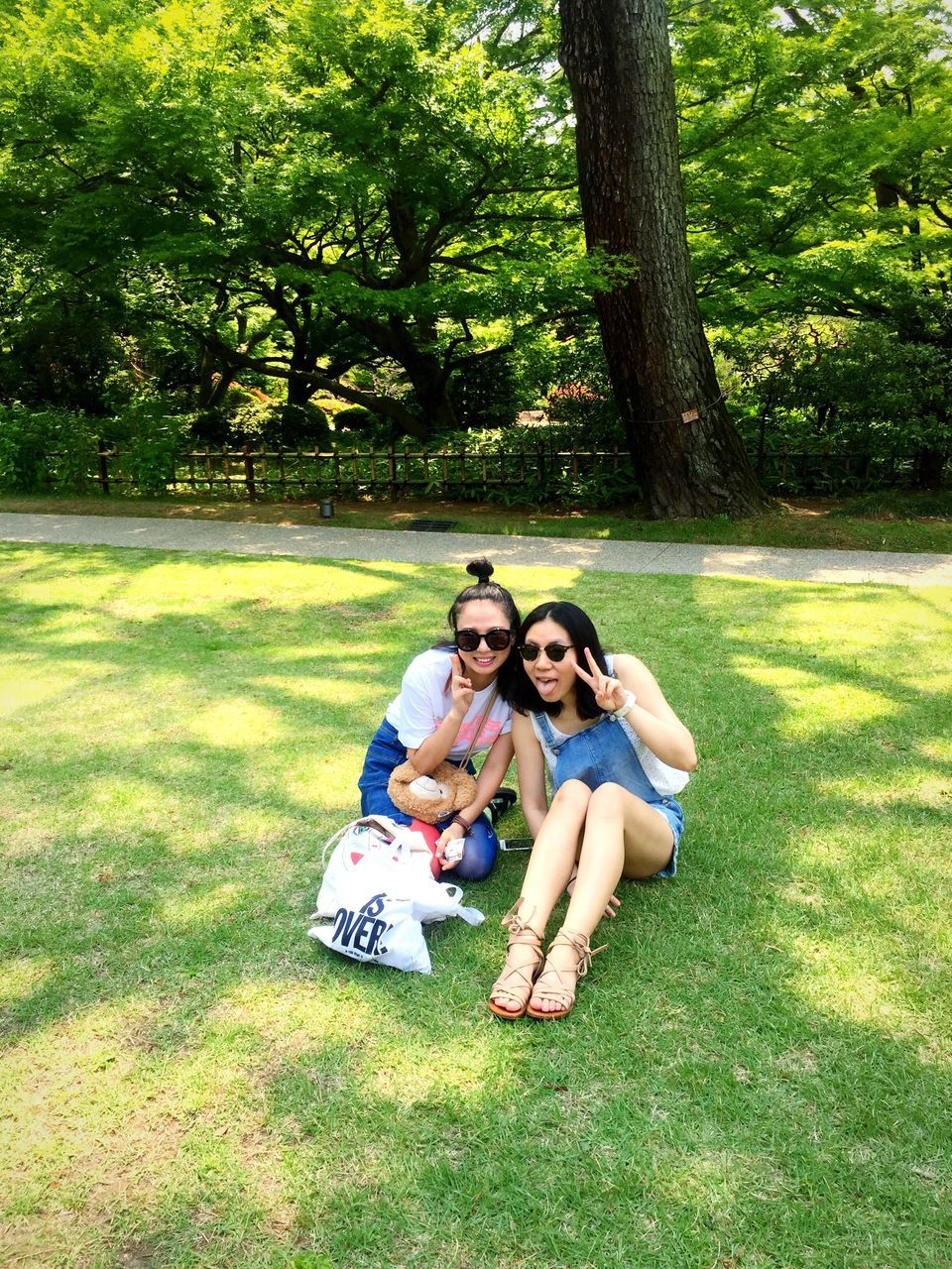 young adult, person, grass, lifestyles, leisure activity, young women, tree, full length, casual clothing, park - man made space, sitting, looking at camera, smiling, happiness, front view, portrait, relaxation, three quarter length