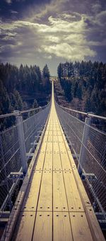 Empty footbridge amidst trees against sky