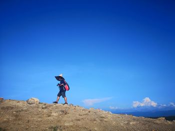 Woman wearing hat walking on mountain against blue sky