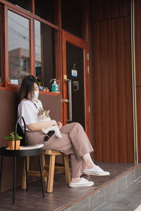 Asian woman wearing protective mask sit and play with her cat at outdoor coffee shop