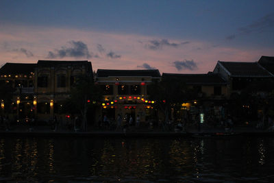 Illuminated buildings by lake against sky at night