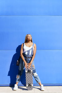 Portrait of young woman standing against blue sky