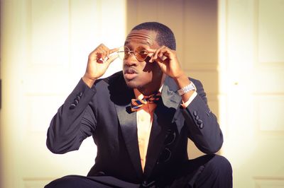 Man holding sunglasses while sitting against wall