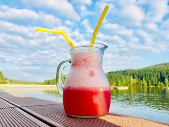 Orange smoothie in a jar with two straws placed on wooden pontoon near the lake