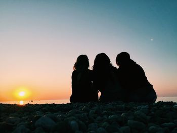 Rear view of friends at beach against sky during sunrise