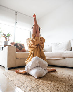 Calm unrecognizable female in sportswear sitting on mat on floor and performing garudasana while practicing yoga at home