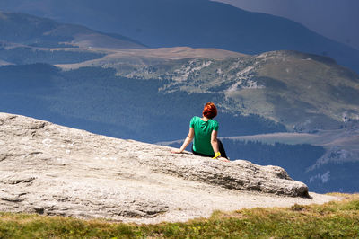 Rear view of woman sitting on mountain in sunny day