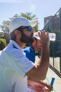 Tennis player drinking water with man while sitting at court