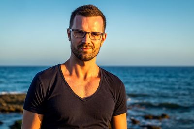 Man wearing eyeglasses while standing at beach against sky