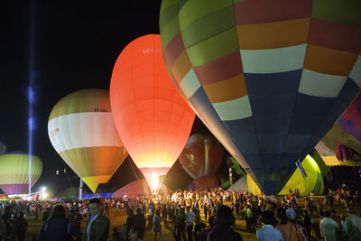 Crowd by hot air balloons on field against sky at night