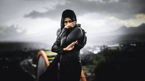 Woman covering mouth while standing on mountain against sky