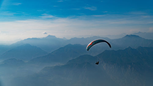 Person paragliding over mountains against sky