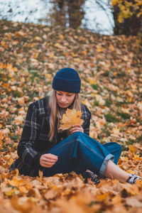 Smiling and happy brunette sitting in a pile of colourful leaves in a city park