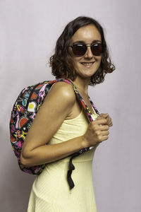 Portrait of smiling young woman wearing sunglasses standing against wall