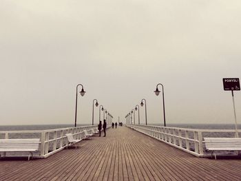 Man walking on railing by sea against clear sky