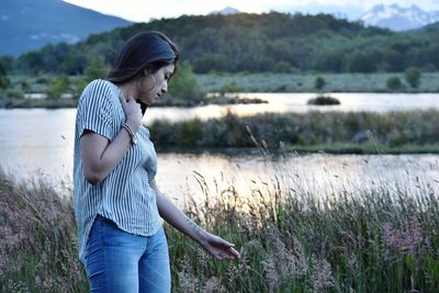 Woman looking at flowers at riverbank during sunset