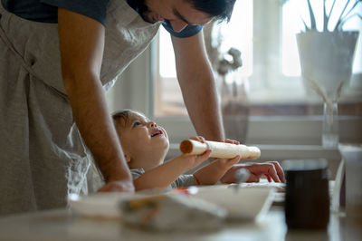 Happy son and father rolling pizza dough in kitchen