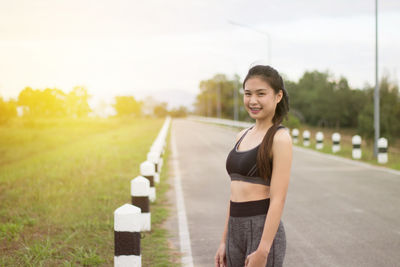 Portrait of smiling young woman standing on road against sky