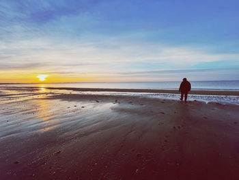 Rear view of woman walking at beach against sky during sunset