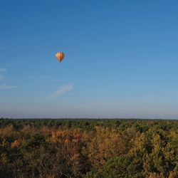 Hot air balloon flying over field against clear blue sky